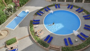 A circular pool with a central water feature surrounded by lounge chairs and a smaller rectangular pool.