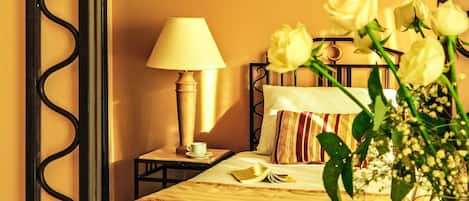 Una cama bien hecha con sábanas blancas, una mesita de noche con lámpara y un jarrón con flores.