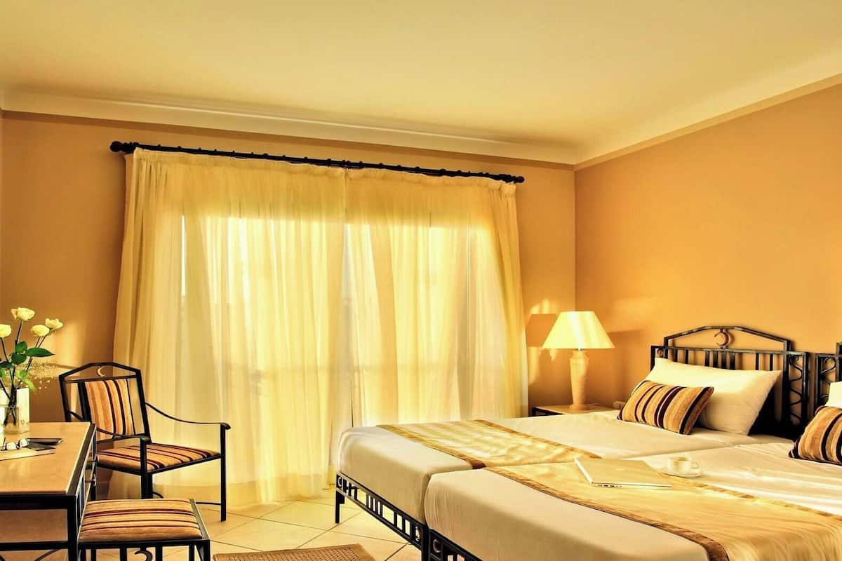 Habitación de hotel con cama, mesitas de noche, lámpara, silla y mesa con un jarrón de flores.