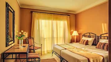 A hotel room with a bed, a desk, a chair, a lamp, and a window with curtains.