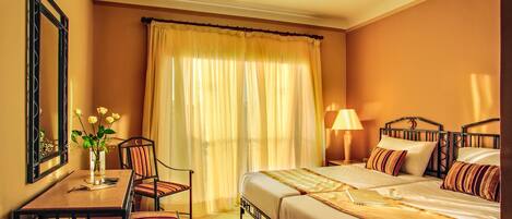 Ein Hotelzimmer mit Bett, Schreibtisch, Stuhl, Lampe und einem Fenster mit Vorhängen.