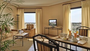 A hotel room with a balcony, a television, a dining table set with breakfast, and a sofa.