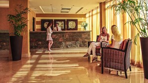 A lobby with a reception desk, seating area, and large potted plants.