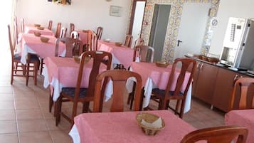 Un comedor con varias mesas cubiertas de manteles rosas, sillas de madera y una máquina de café.