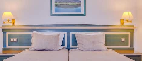 Ein Doppelbett mit Kopfteil, zwei Nachttischlampen und ein gerahmtes Landschaftsbild an der Wand.