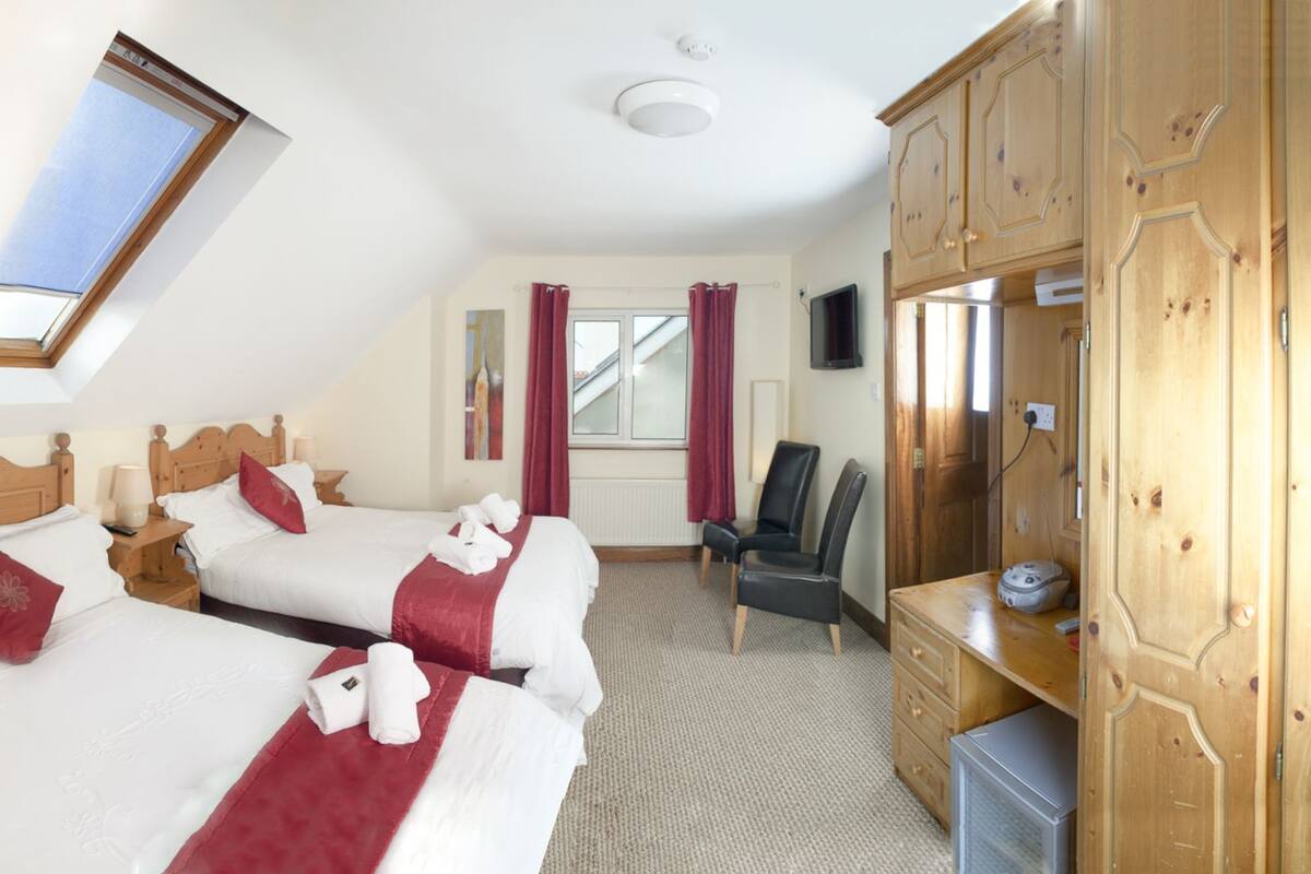A hotel room with two beds, a desk, a chair, and a TV.