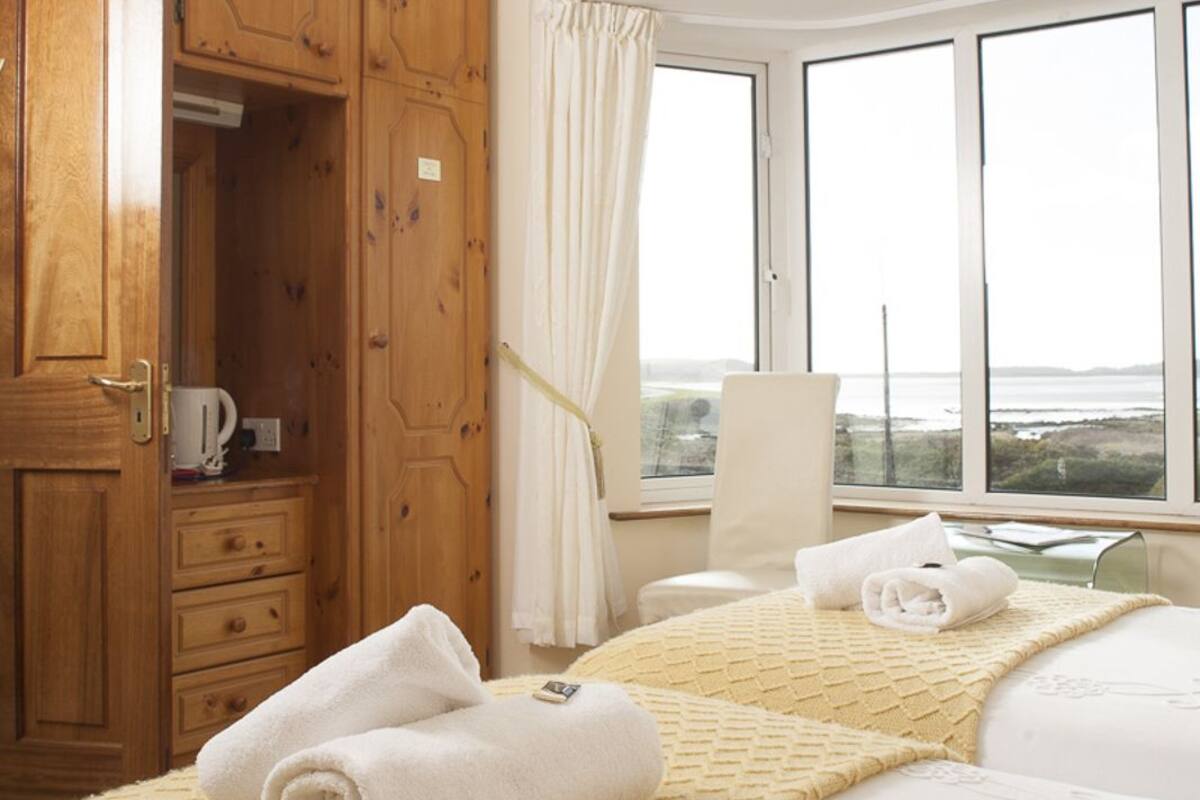 A hotel room with two beds, a wooden wardrobe, a chair, and a large window with a view.