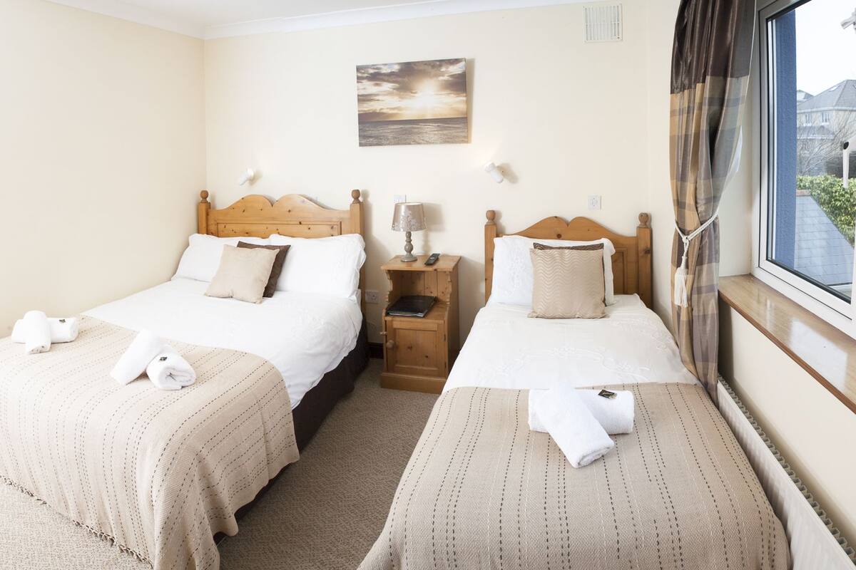 A hotel room with two beds, a nightstand, a lamp, and a painting on the wall.