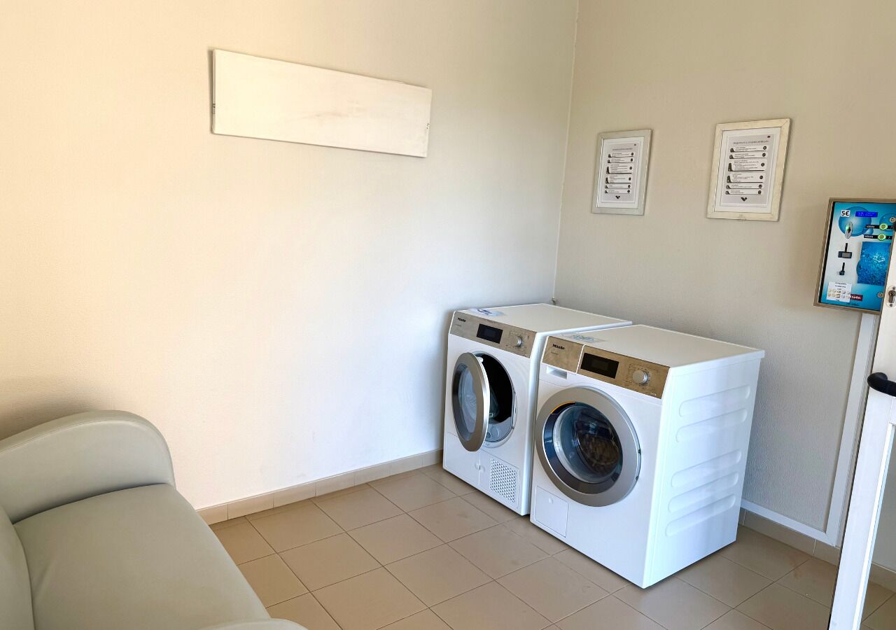 A laundry room with two stacked washing machines, a light-colored sofa, and a wall-mounted control panel.