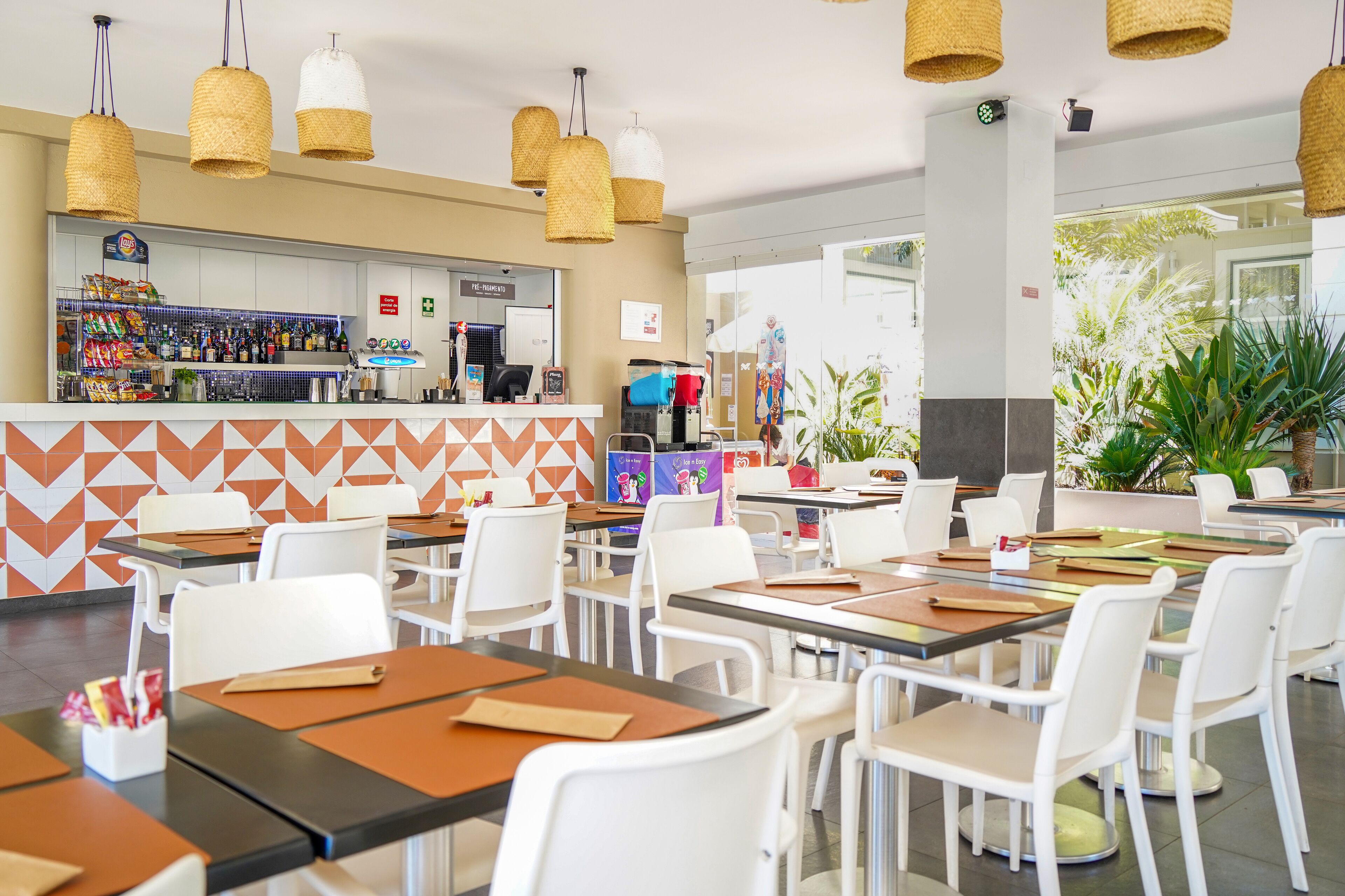 A restaurant with white chairs and tables, a counter with snacks, and hanging wicker lamps.