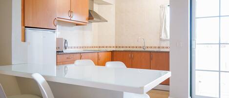 A modern kitchen with wooden cabinets, a white countertop, and a glass dining table.