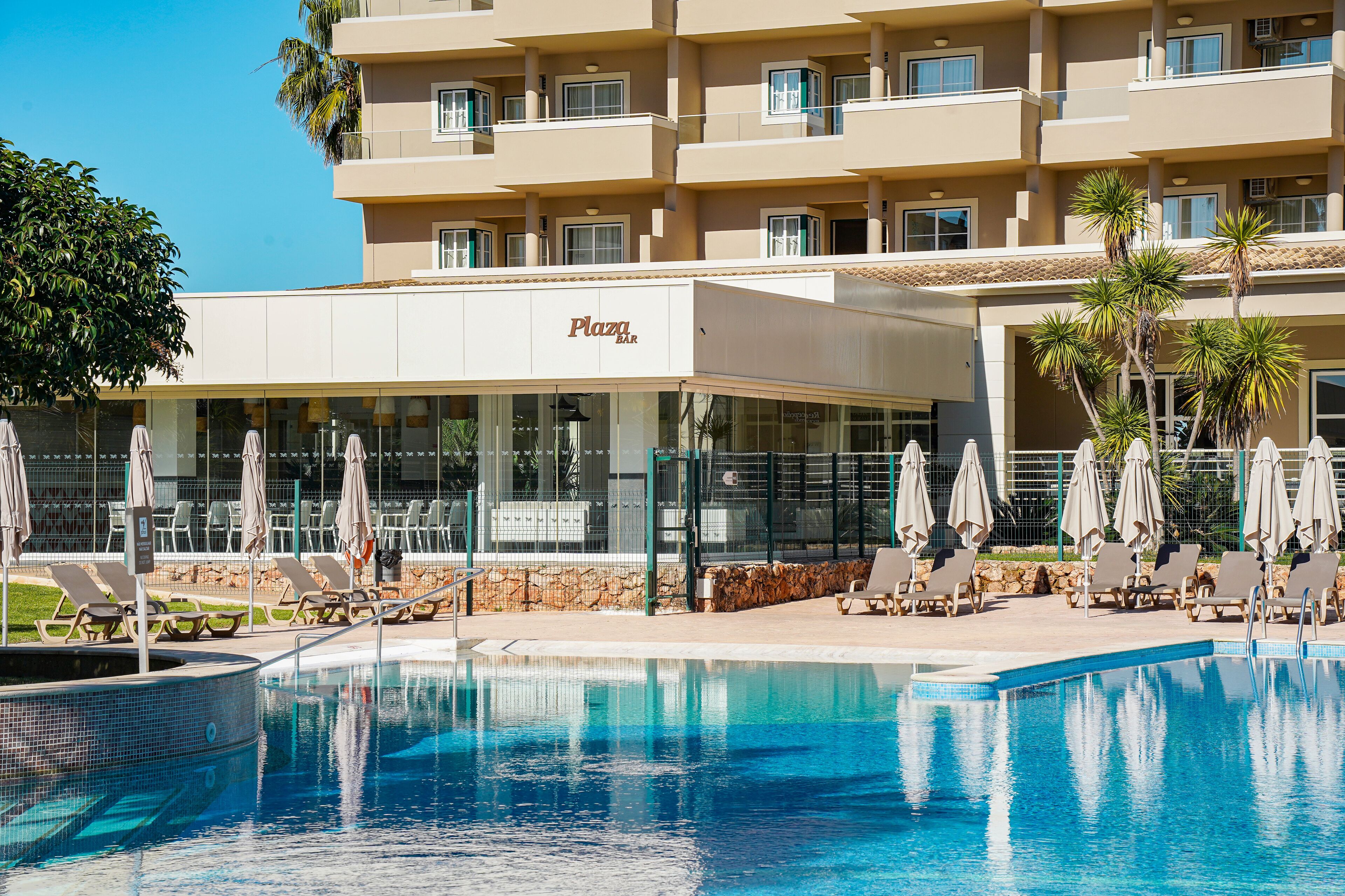 A hotel with a pool area, sun loungers, and umbrellas.