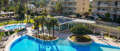 A swimming pool with lounge chairs and palm trees, surrounded by multi-story buildings.