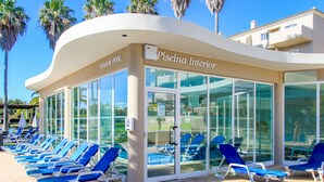 A poolside area with blue lounge chairs and a glass-enclosed building labeled "Piscina Interior." - Vitors Plaza (Portimão)
