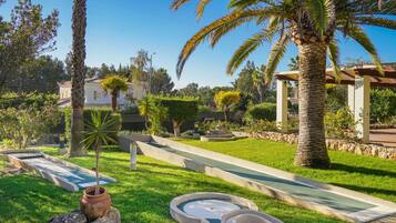 Un jardín bien cuidado con una palmera, un pequeño estanque y un sendero empedrado.
