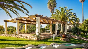 A covered outdoor area with a pool, palm trees, and a stone wall. - Vitors Plaza (Portimão)