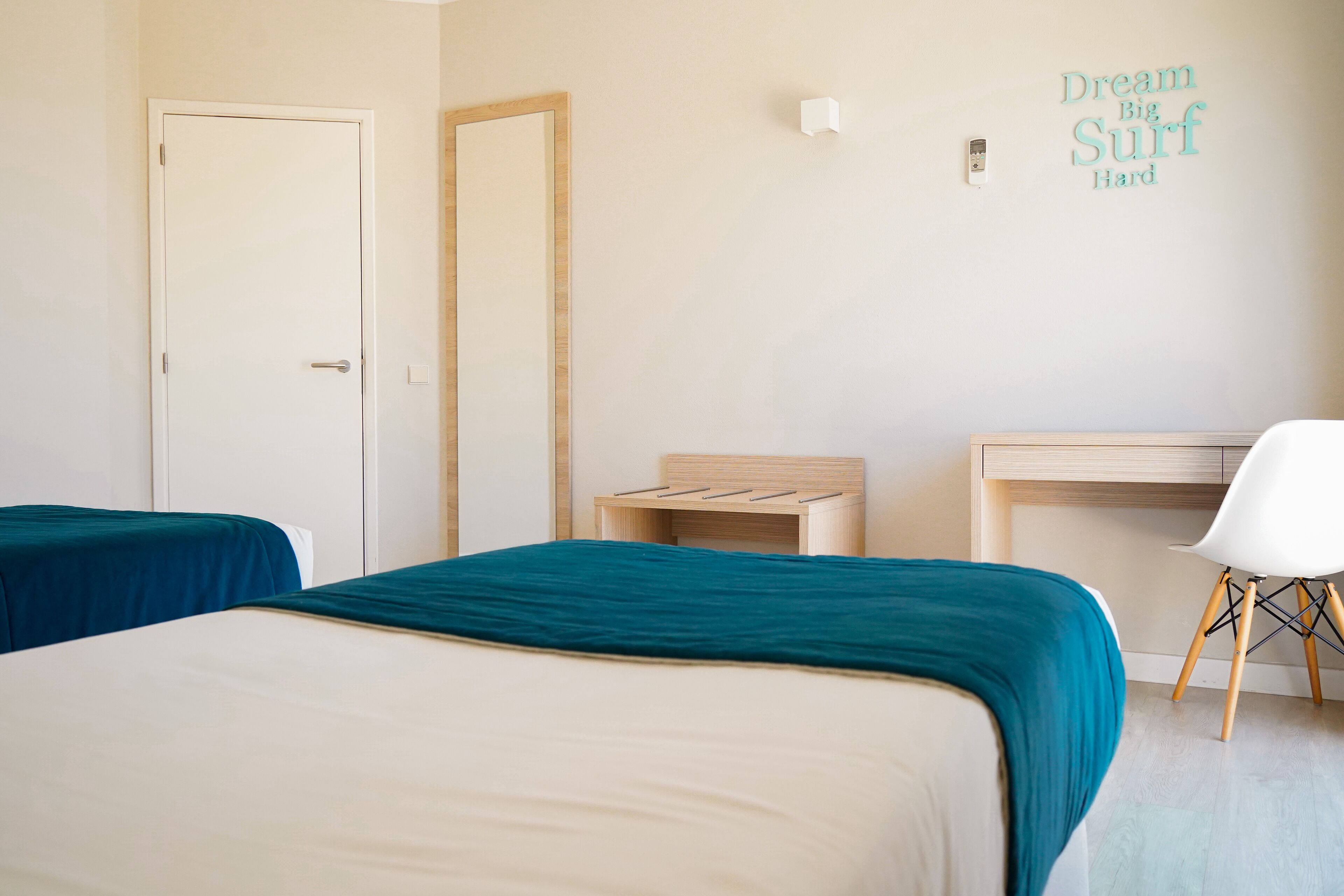 A hotel room with two beds, a desk, a chair, and a wall with motivational text.