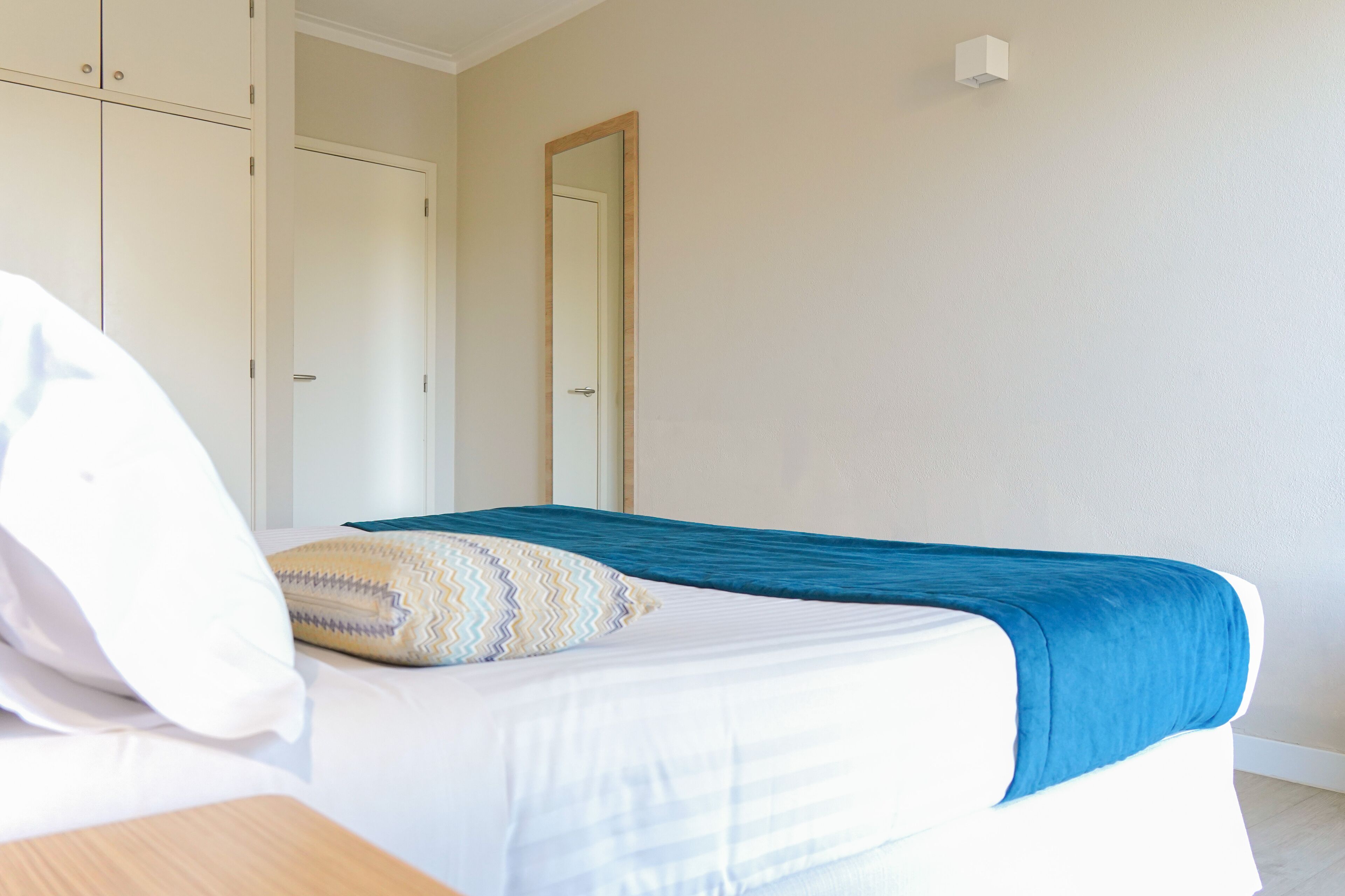 A bedroom with a bed, a bedside table, a wardrobe, and a mirror.