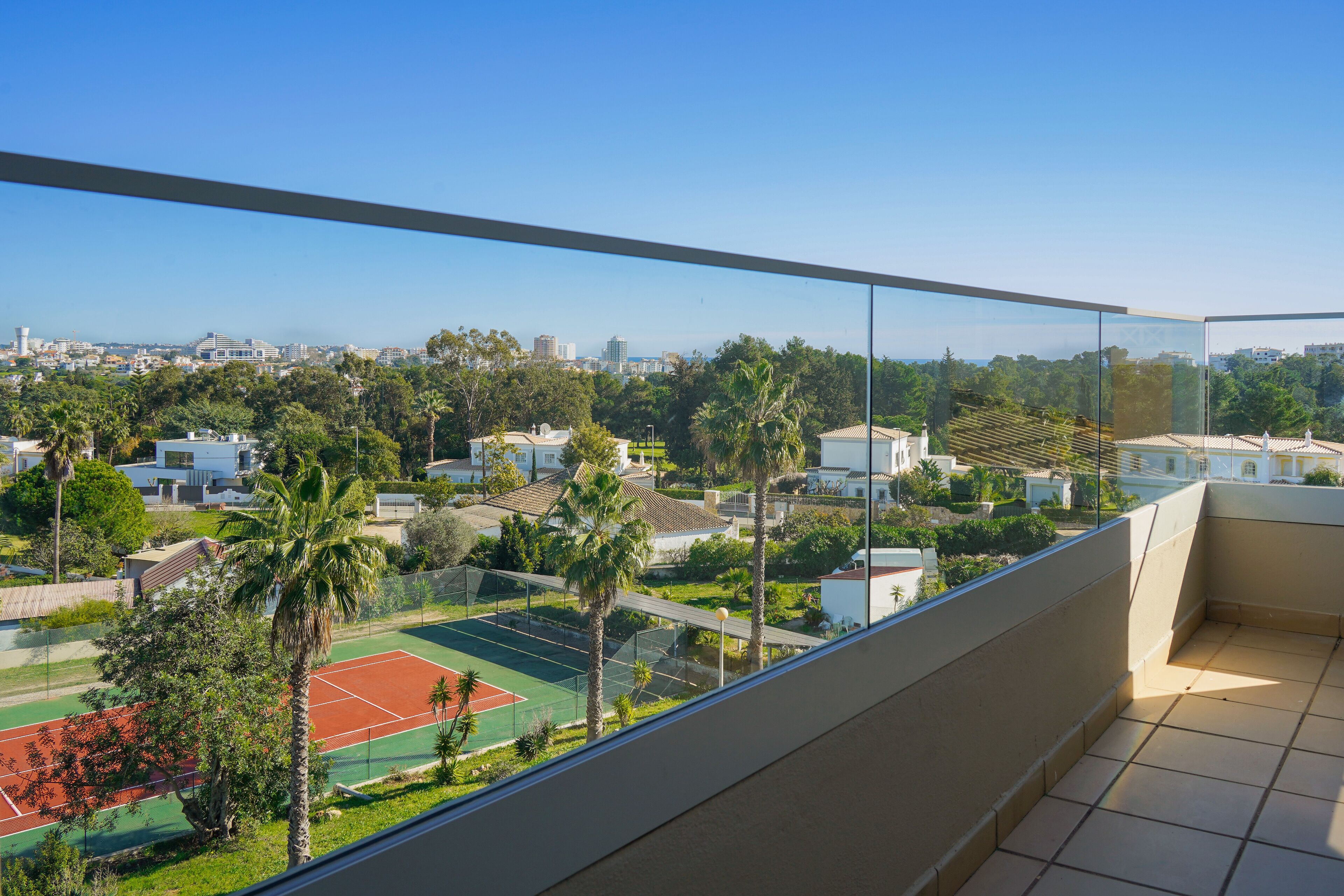 Un balcó amb vista despejada a una pista de tennis, palmeres i edificis residencials.