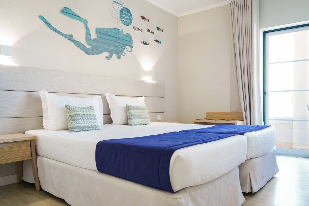 Ein Hotelzimmer mit zwei Betten, einem großen Fenster und einem Wandgemälde.