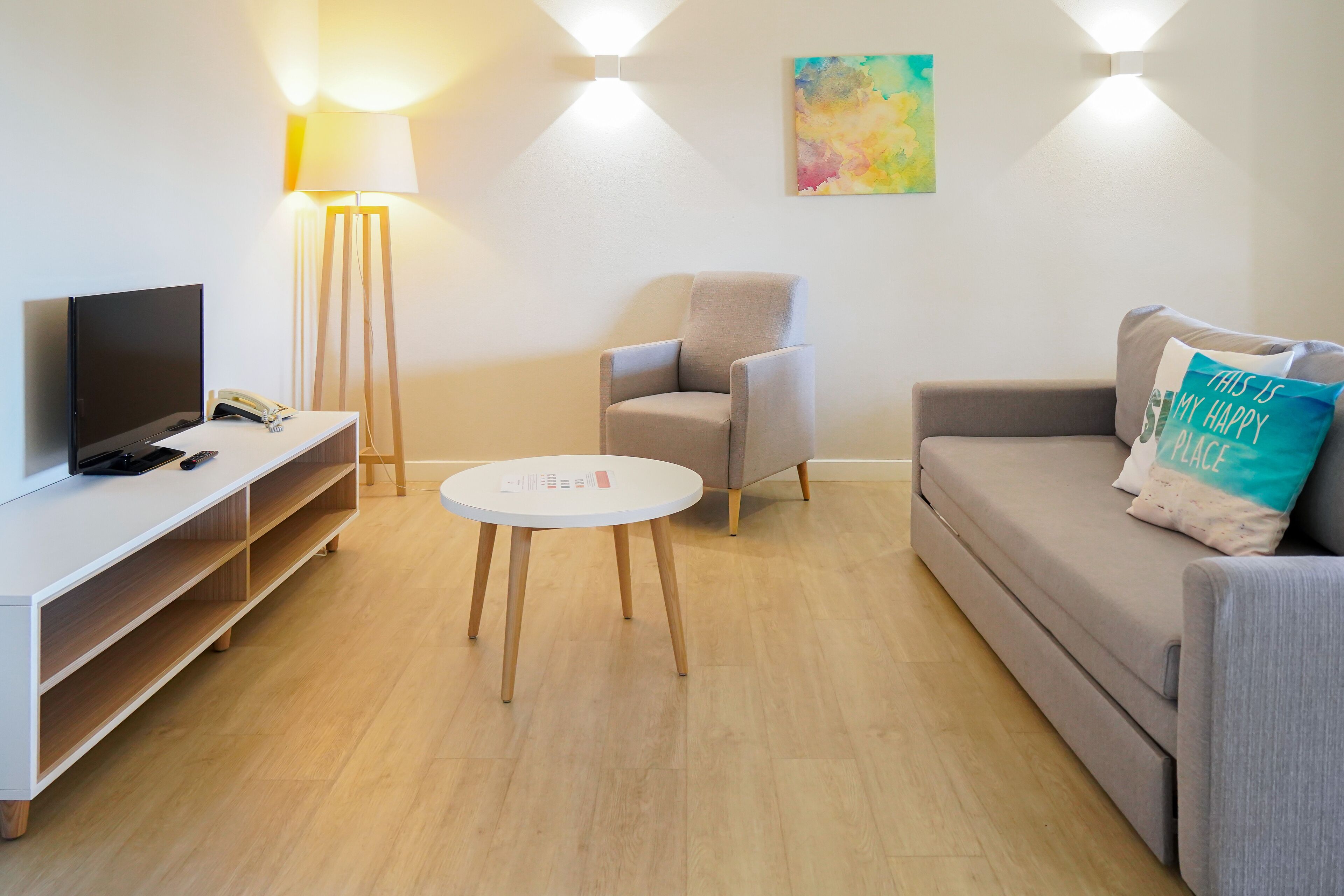 A modern living room with a flat-screen TV, a round coffee table, a grey sofa, and a chair.