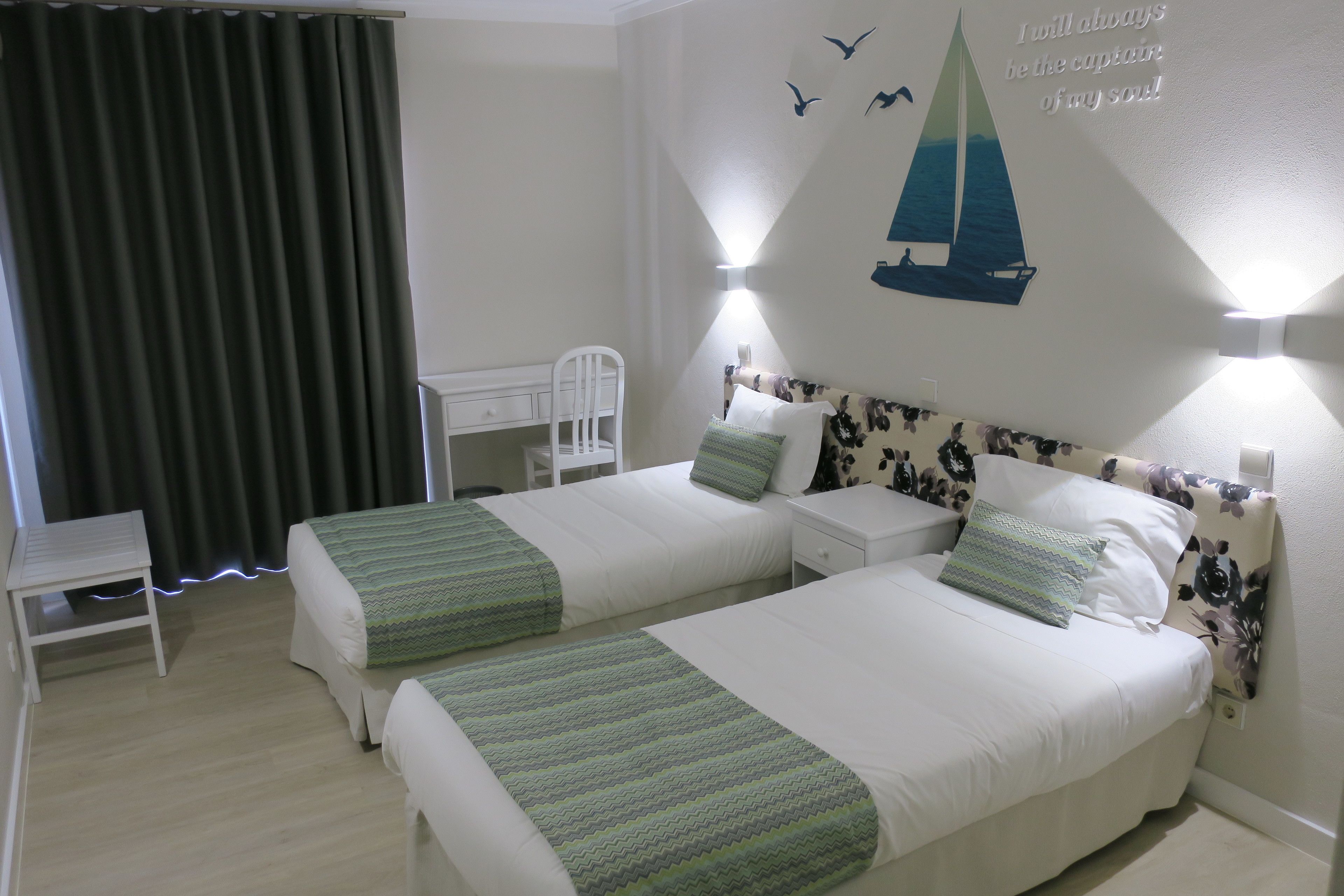 A hotel room with two single beds, a desk, and a chair.