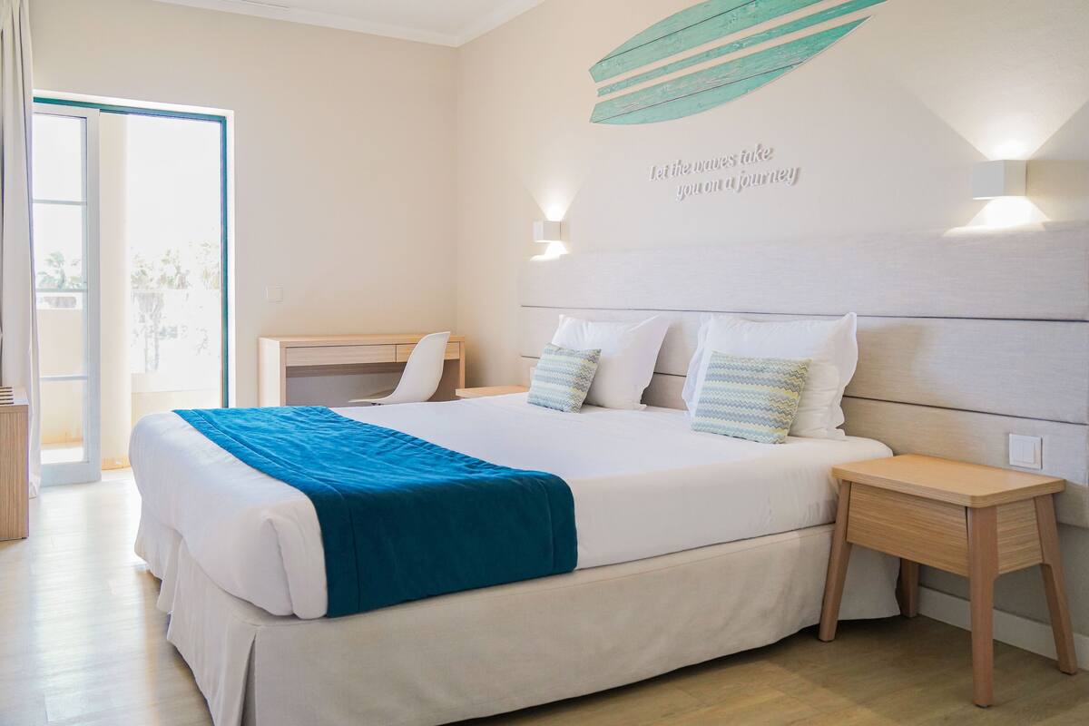 Ein Schlafzimmer mit einem Bett, Nachttischen, einer Wand mit Dekoration und einer Tür zum Balkon.