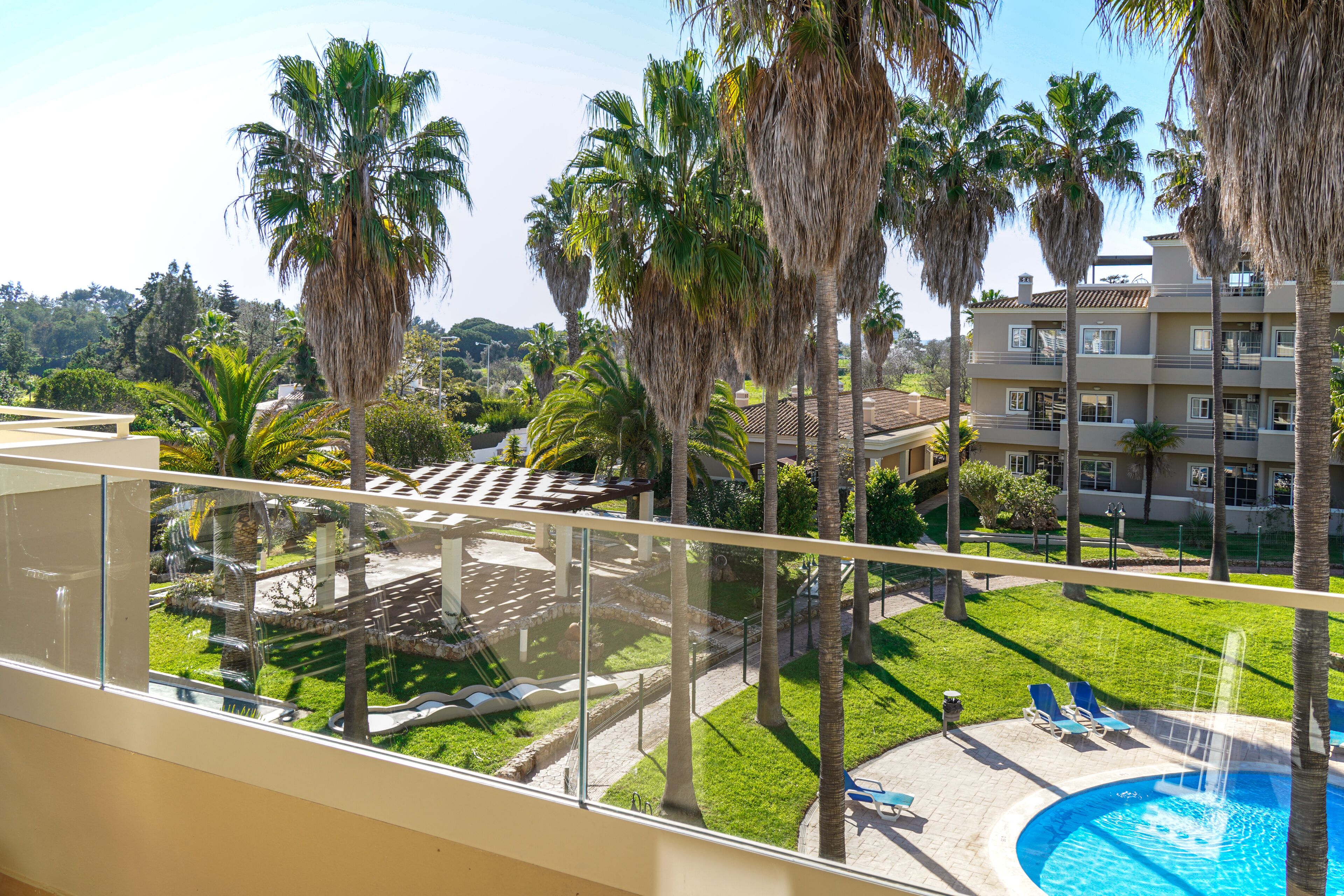 Un balcon donnant sur une piscine, des palmiers et un immeuble doté de nombreux balcons.