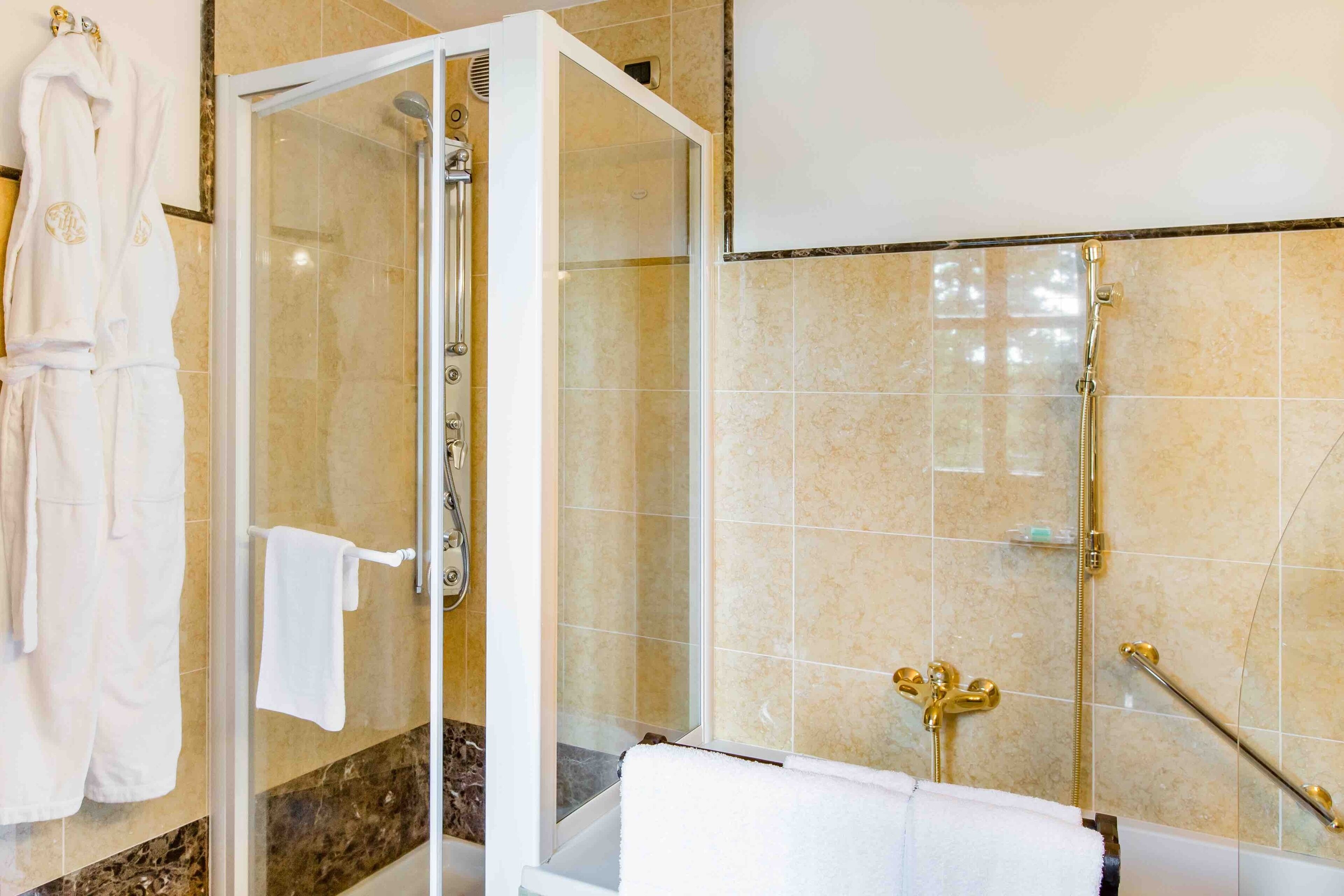 A modern bathroom with a glass-enclosed shower, a bathtub with gold fixtures, and a white towel rack.