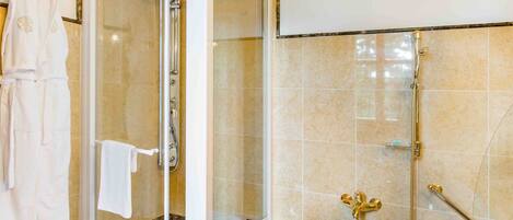 A modern bathroom with a glass-enclosed shower, a bathtub with gold fixtures, and a white towel rack.