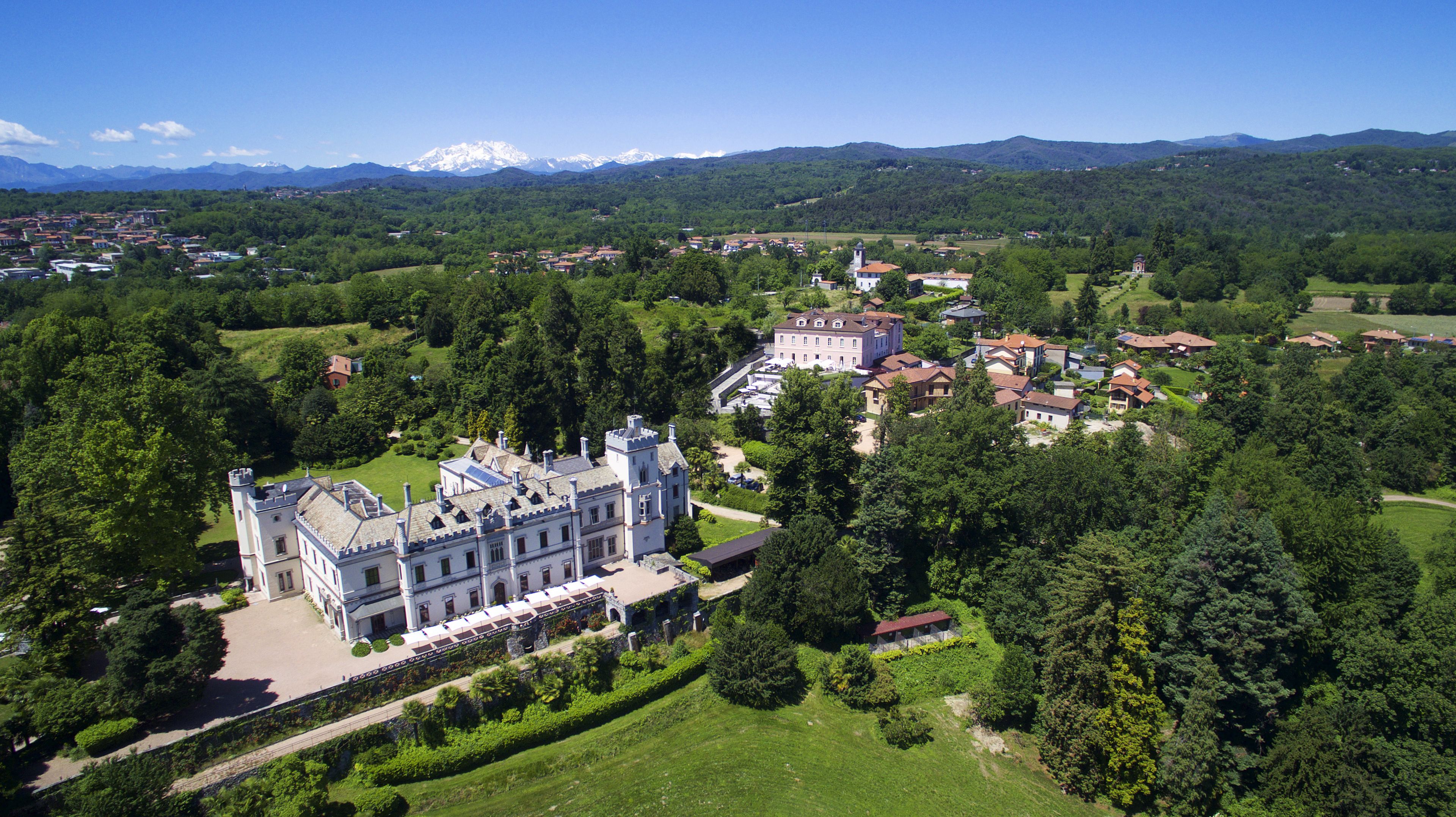 Um edifício grande e histórico com fachada simétrica, rodeado por vegetação exuberante e um gramado bem cuidado.
