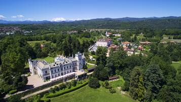 Um edifício grande e histórico com fachada simétrica, rodeado por vegetação exuberante e um gramado bem cuidado.