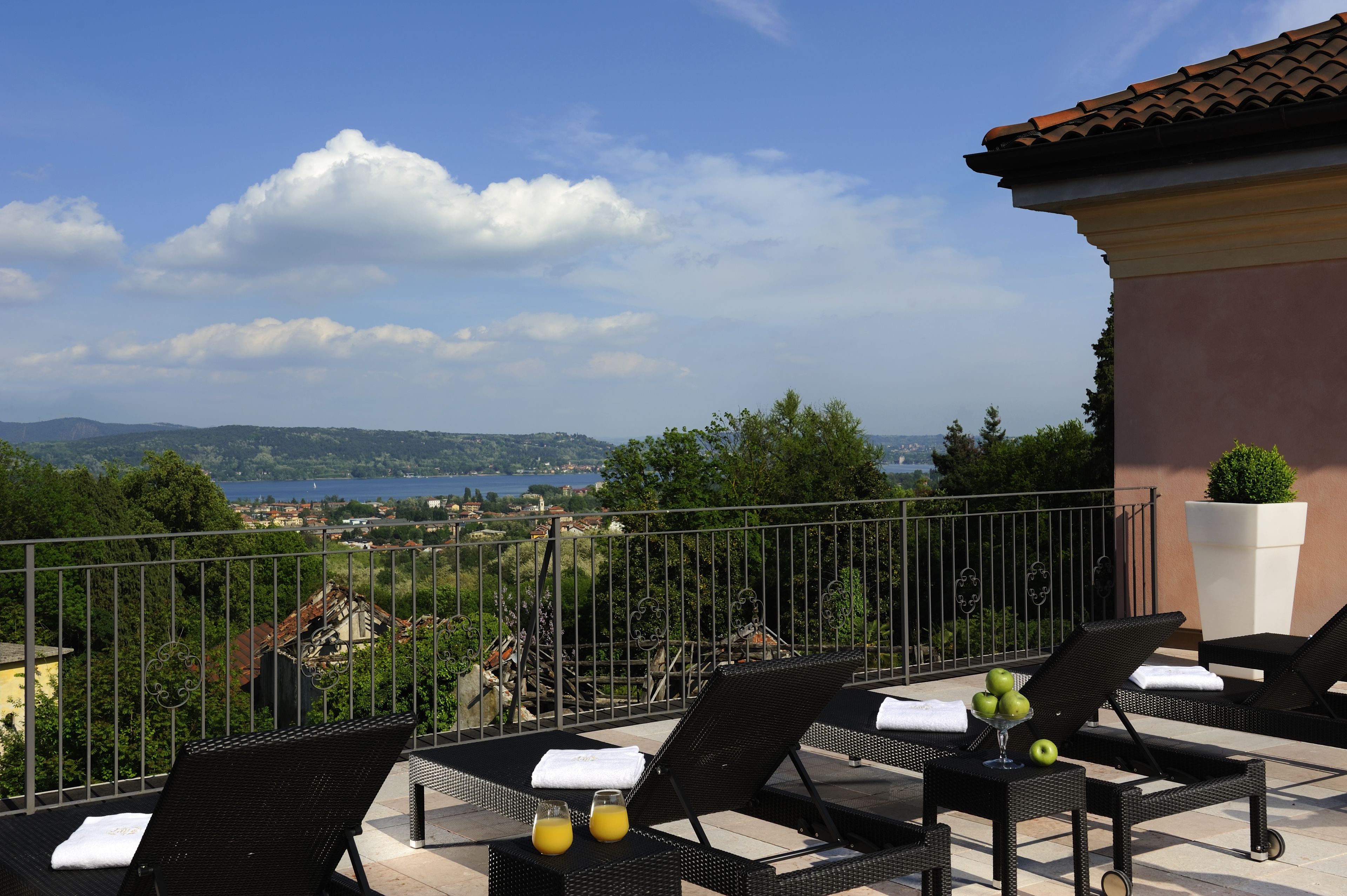 A balcony with lounge chairs, a table with a drink, and a view of a town and lake.