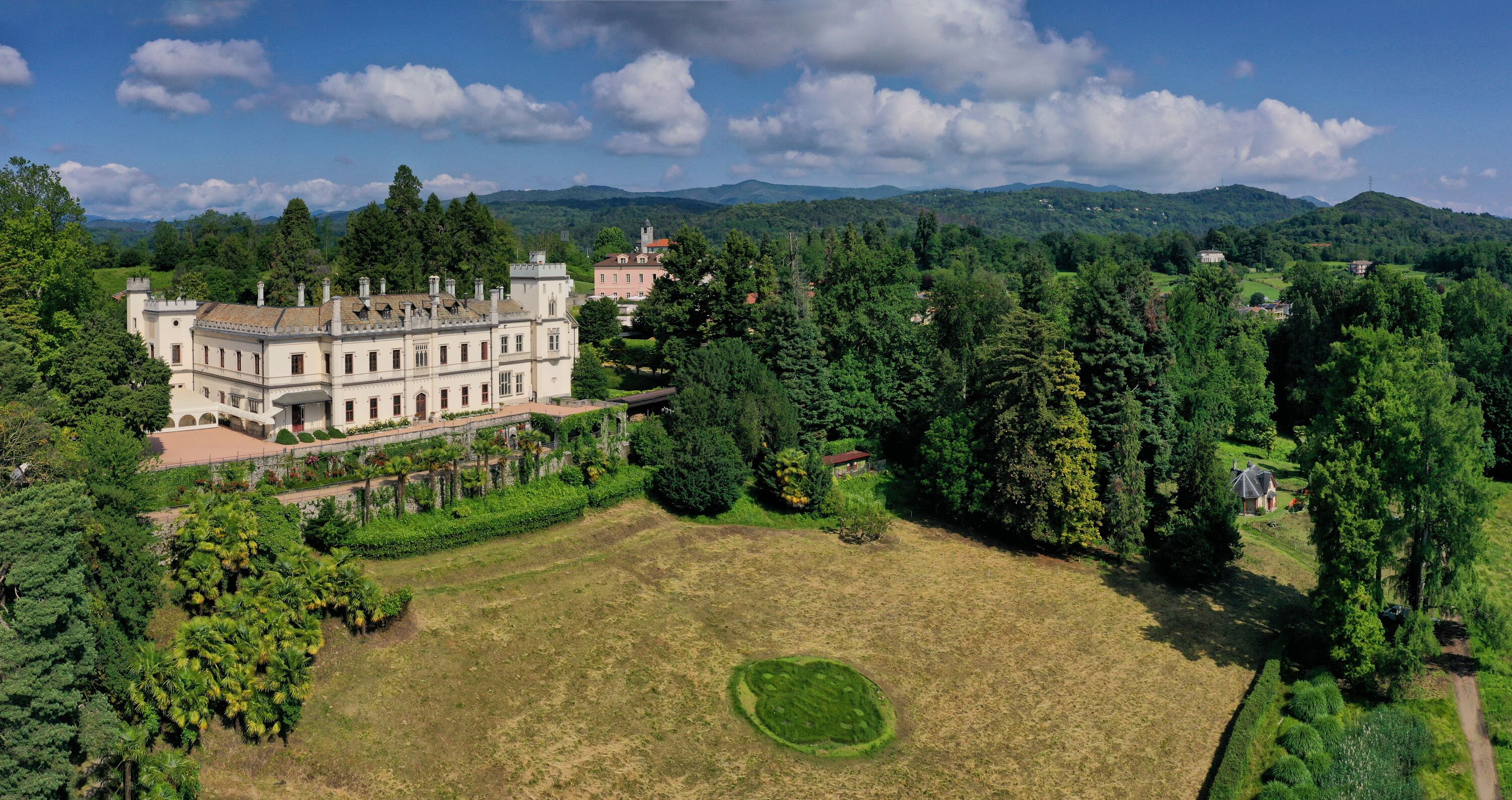 Un grand bâtiment historique doté de plusieurs ailes et d’une cour spacieuse, entourée d’une végétation luxuriante et d’arbres.