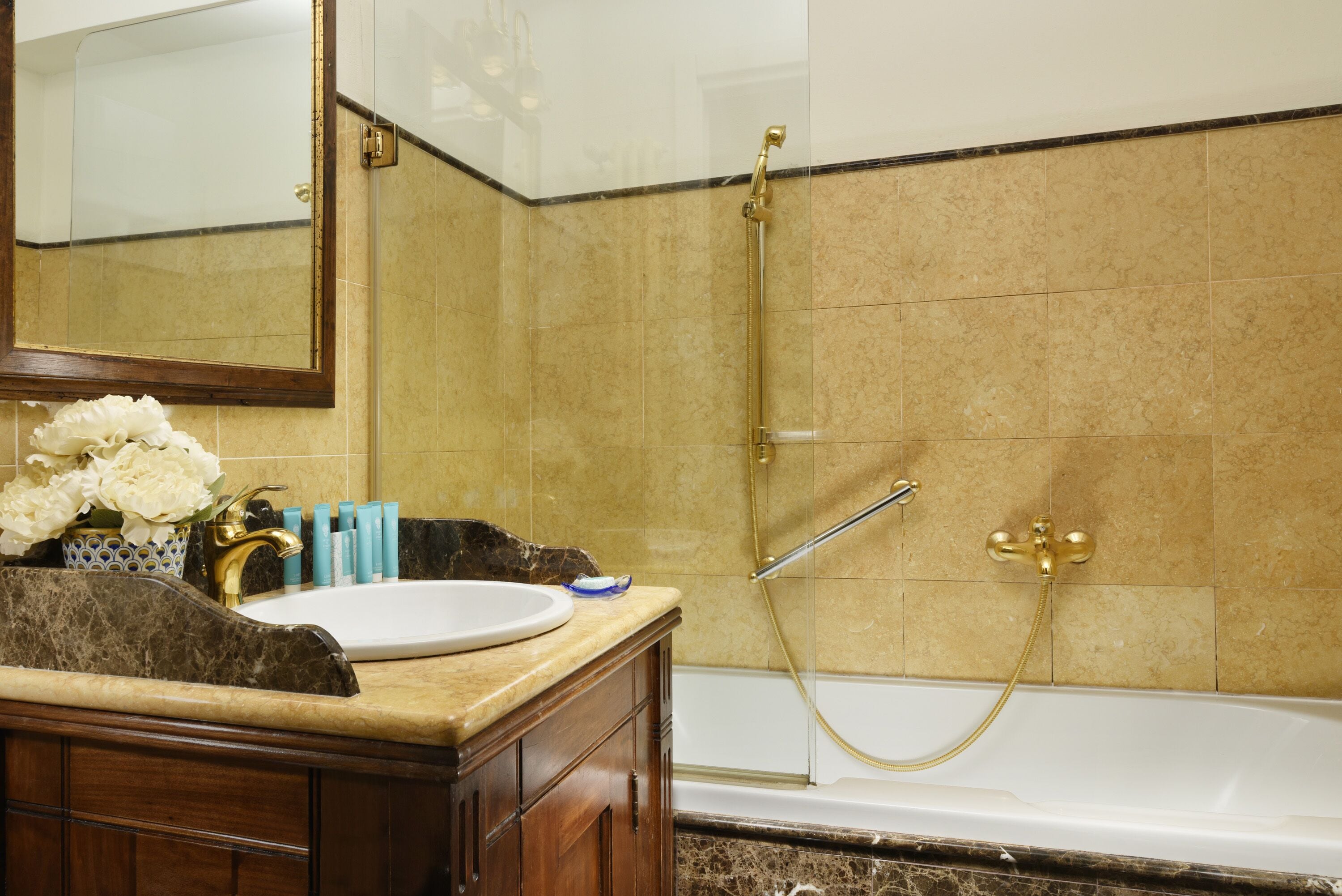 A bathroom with a marble sink, gold fixtures, and a bathtub.