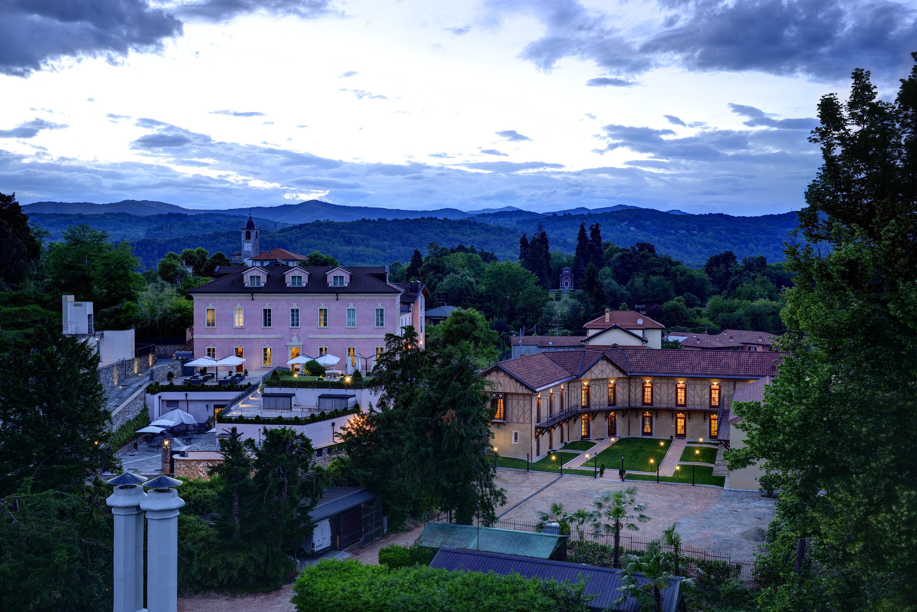 A large, multi-story building with a prominent tower, surrounded by lush greenery and mountains in the background.