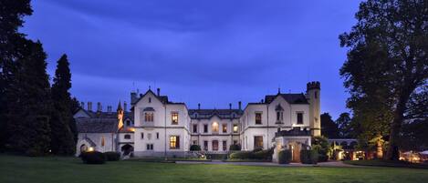 A large, historic building with multiple towers and a well-maintained lawn in front.