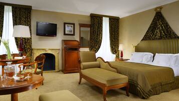 Quarto de hotel com cama, poltrona, mesa com um vaso, televisão e lareira.