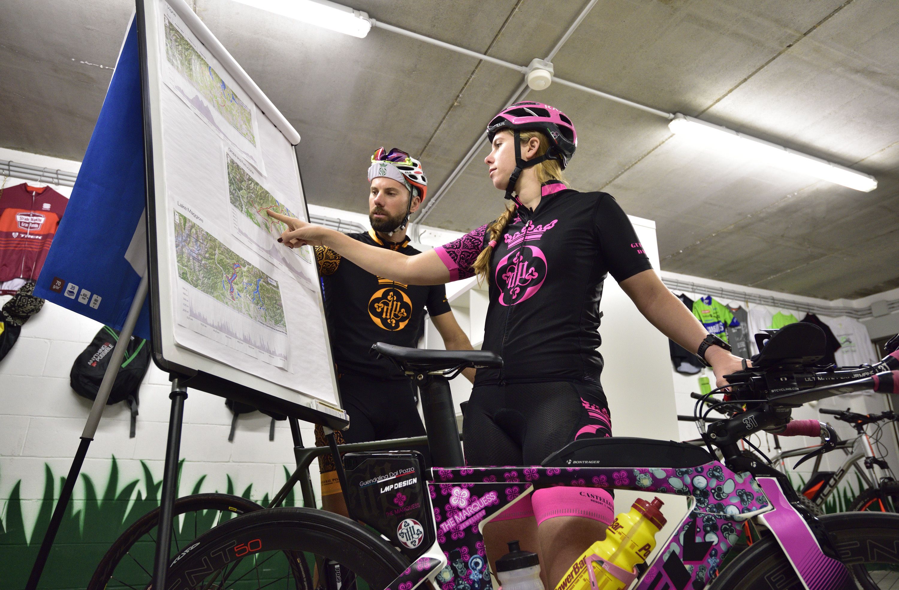 Due persone che esaminano una mappa in una stanza con biciclette e una bandiera appesa al muro.