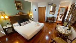 Habitación de hotel con una cama grande, piso de madera, un área de descanso con una mesa y sillas, y un espejo.