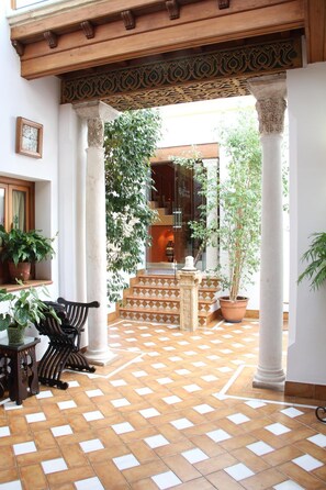 Un patio con suelo de baldosas, plantas en macetas y un banco.