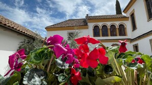 Un edificio con tejado de baldosas y ventanas de arco, rodeado de flores rosas vibrantes.