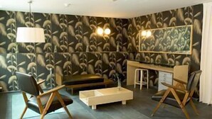 Une pièce moderne avec un papier peint à motifs sombres, un bureau avec un miroir, deux chaises, une petite table et un luminaire suspendu.