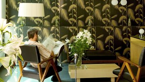 Une pièce avec un papier peint à motifs, une table basse en verre et un fauteuil sur lequel est posé un livre.