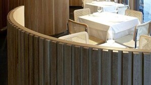 Un restaurant doté d’une cloison en bois aux lignes courbes, de tables et de chaises blanches.