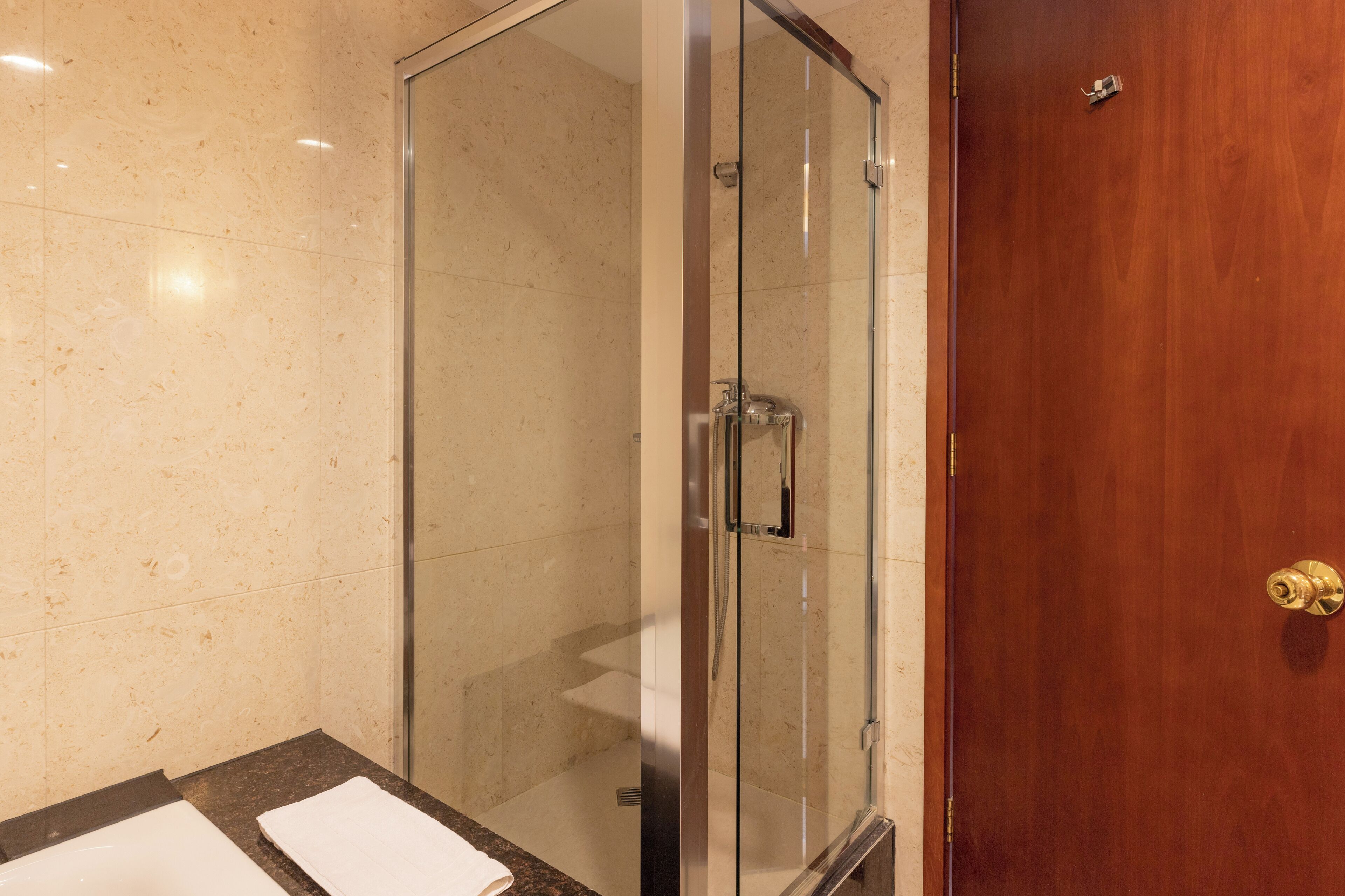 Eine begehbare Glasdusche mit Holztür, eine Wand mit Marmorplatten und eine schwarze Ablage mit einem weißen Handtuch.