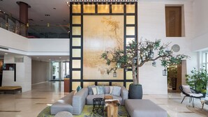 A spacious lobby with a large sectional sofa, a round coffee table, and a potted tree. - Shanghai Hotel Holland (Delft)
