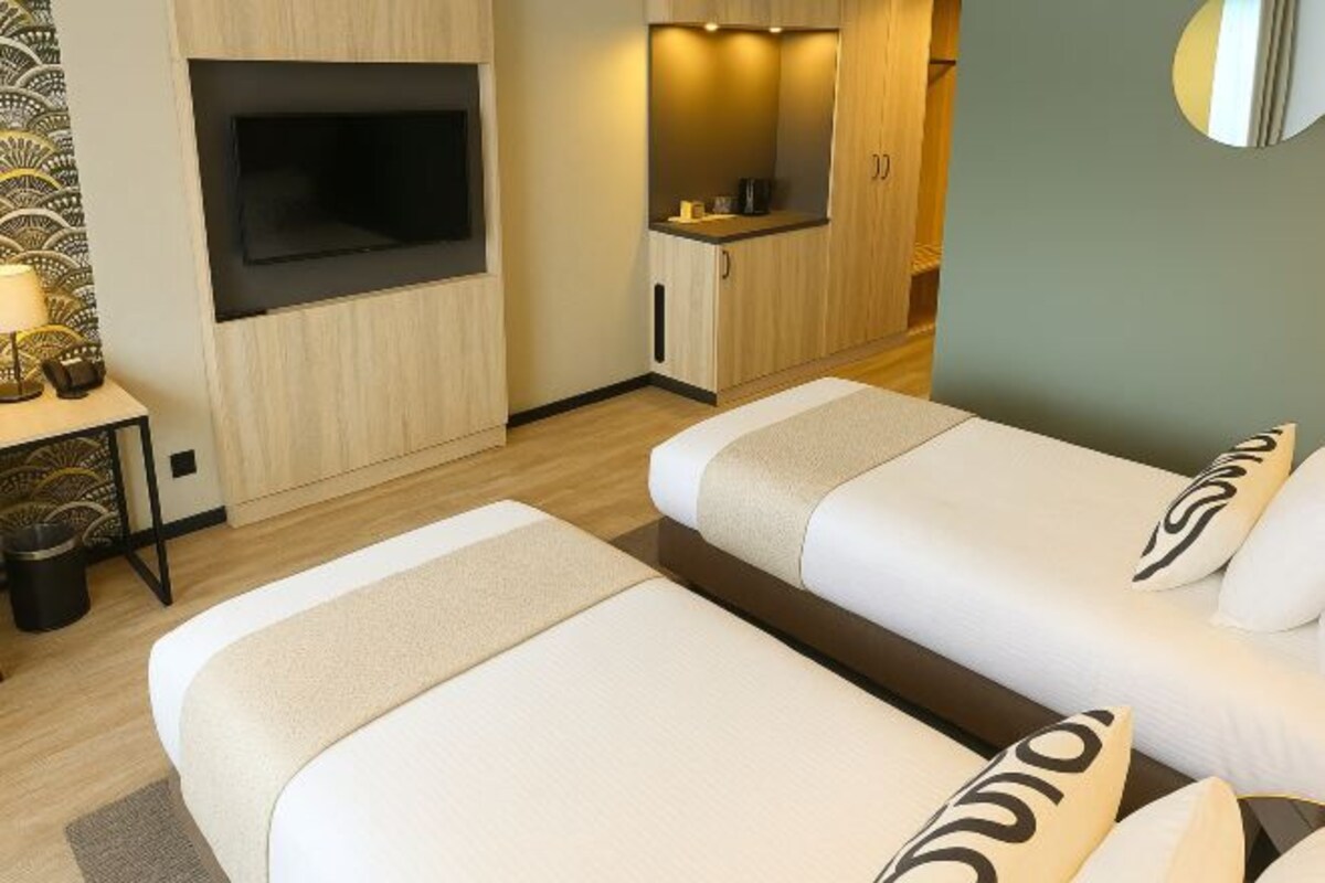 A hotel room with two beds, a TV, a small kitchenette, and a mirror.