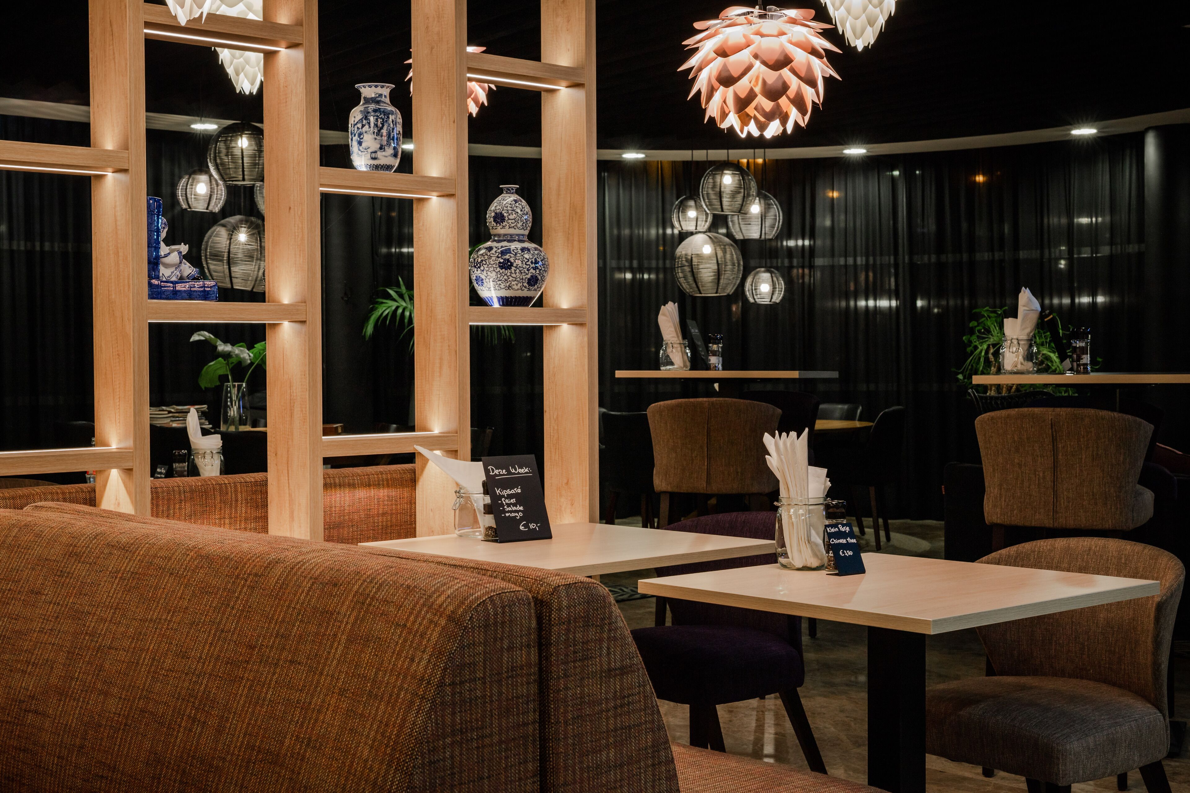 A restaurant interior with wooden paneling, cushioned seating, and decorative lighting.
