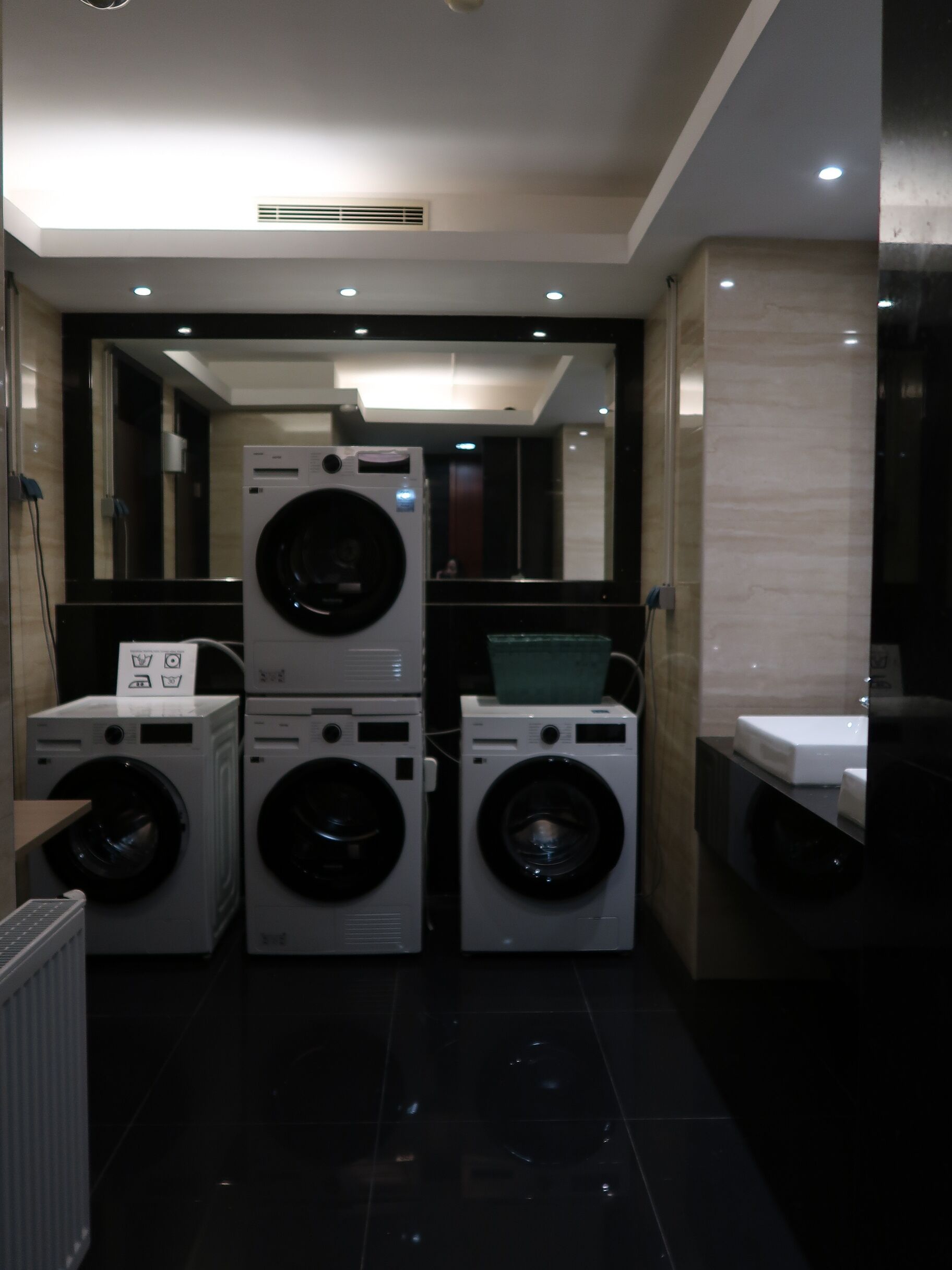 A modern laundry room with stacked washing machines, a mirror, and a sink.